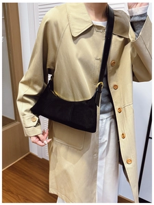 Detail of black suede hobo bag with adjustable gold buckle strap on khaki trench coat