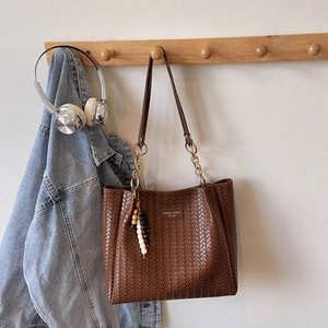 Gros plan détaillé du sac cabas tressé marron avec logo en métal et breloque perlée