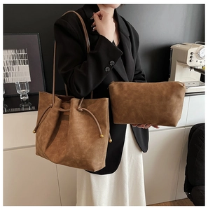 Detail view of brown matte leather tote bag and zipper pouch shown on a model indoors