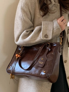 Polished dark brown leather tote bag with shoulder strap and wooden bead charm accessory