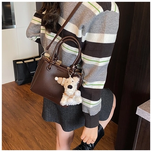 Detail of a dark brown pebble leather tote bag with a white plush dog charm on handle