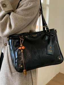 Chic black leather tote bag for women featuring vintage texture and orange tassel detail