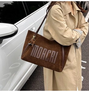 Detail of a brown suede tote bag with MOACRI embossing and a horse leather charm