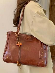 Classic brown leather tote bag with gold logo and bead tassel on shoulder