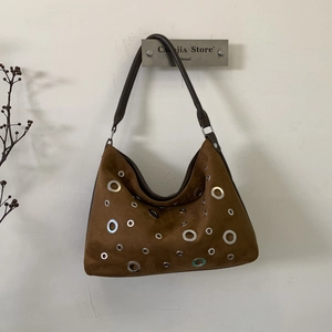 Detail of a brown suede shoulder bag featuring silver metal eyelet hollow-out design