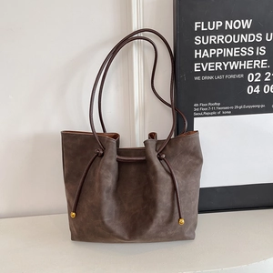 Detail of dark brown matte leather tote bag featuring drawstring and gold metal bead