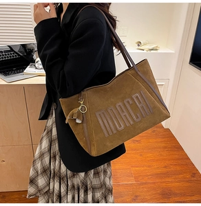 Detail view of brown suede tote bag with MOACRI embossed logo and decorative tassel