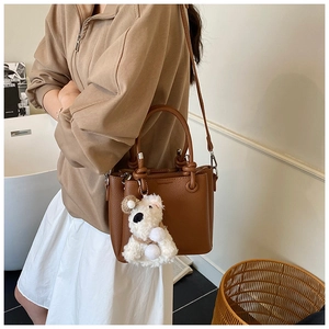 Chic brown lychee leather handbag with a cute white puppy pendant in a lifestyle setting