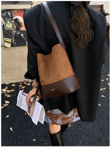 Detail of a brown leather bucket bag with contrasting textures and gold brand logo