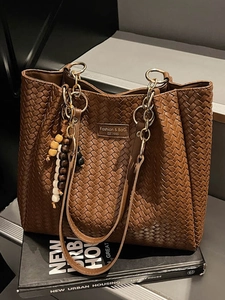 Sac cabas tissé marron avec bandoulière en chaîne et pendentif perlé sur fond urbain chic