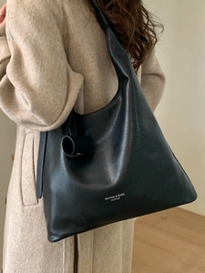 Grand sac hobo en cuir noir avec lettrage blanc porté sur un manteau en laine beige
