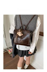 Close-up of vintage dark brown faux leather backpack with plush bear charm and embossed logo