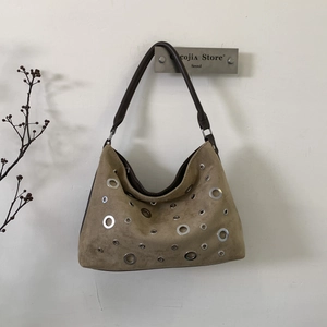 Retro suede hobo bag with silver eyelets hanging on a hook with minimalist decor