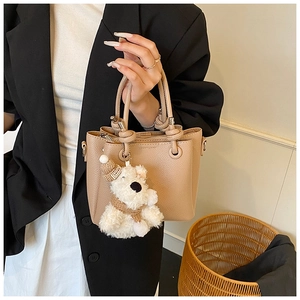 Detail of minimalist beige bucket bag with litchi texture and cute plush bear charm