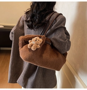 Dettaglio della borsa tote in peluche marrone con manici in pelle e ciondolo a orsetto