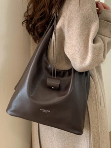 Sac Hobo minimaliste en cuir marron foncé porté en bandoulière par un mannequin
