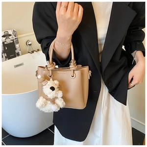 Detail of khaki pebbled leather handbag with cute plush bear charm and metal hardware