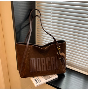 Detail of dark brown faux suede tote bag with MOACRI embossing and elephant charm