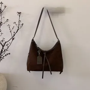 Détail du sac lune vintage en daim marron foncé avec pompon et bandoulière fine suspendu
