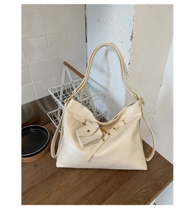 Detail view of cream-white faux leather tote with golden rivets and mini hanging pouch