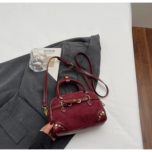 Detail view of burgundy leather and suede stitching on retro handbag with gold rivets