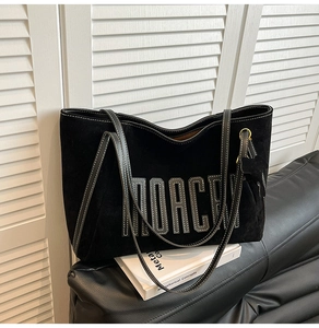 Detail of black suede tote bag with MOACRY patch and white contrast stitching on the strap