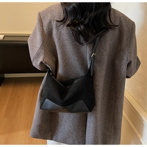 Detail of minimalist black crossbody bag with gold buckle and textured leather materials