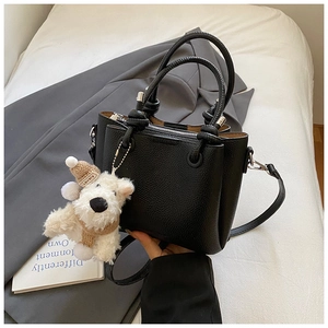 Close-up of black lychee leather handbag with cute plush puppy charm on a blazer background