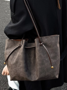Vintage dark gray tote bag with brown cord straps shown in an outdoor street style shot