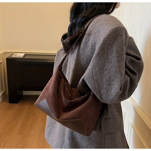 Detail of dark brown suede shoulder bag worn with a grey suit in a stylish interior