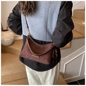 Detail view of dark brown suede half-moon bag with wooden bead tassels and metal logo