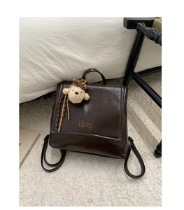 Close-up of retro brown PU leather backpack with gloss finish and cute plush bear charm