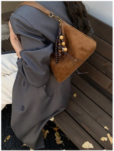 Close-up of vintage brown suede shoulder bag with wooden bead charm in autumn setting