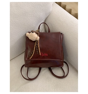Detail of burgundy leather backpack with lbm embroidery and cute plush bear charm