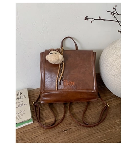 Close-up of vintage brown leather backpack with bear charm and embroidery detail