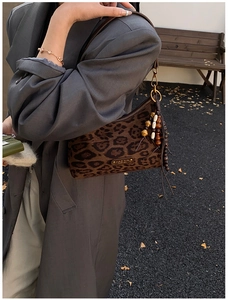 Detail view of leopard print baguette bag with golden logo and wooden beaded tassel charm