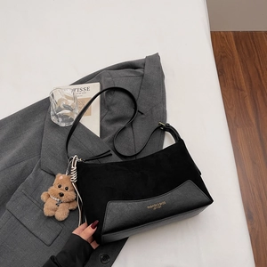Close-up of black crossbody bag with stylish teddy bear charm on grey blazer backdrop