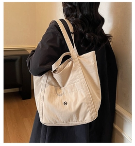 Close-up of a cream-colored large capacity tote bag featuring an outer pocket and logo
