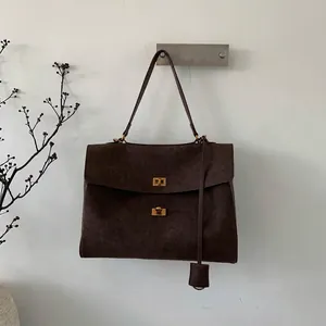 Detail of dark brown suede tote bag featuring dual golden metal twist locks and leather tag