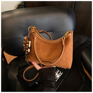 Detail of vintage brown suede shoulder bag with wooden bead charm and embossed logo tag