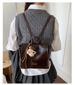 Detail view of dark brown vintage backpack with shiny finish and cute teddy bear charm