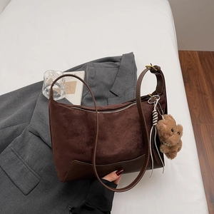 Detailed close-up of dark brown suede crescent bag with plush bear charm accessory