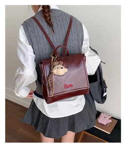 Detail view of burgundy leather backpack with cute teddy bear charm and embroidery