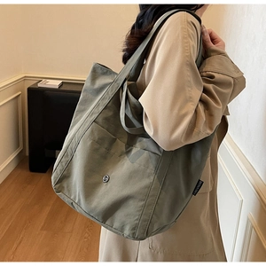 Detail of olive green canvas tote bag with metal logo and side pocket on model