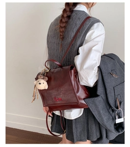 Detail of burgundy leather backpack with ibn embroidery and a cute plush bear charm