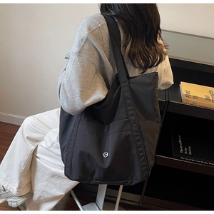 Model wearing a black canvas tote bag with a CM logo in a minimalist industrial setting