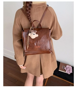 Detail shot of a brown vintage leather backpack featuring a plush bear charm on a female model