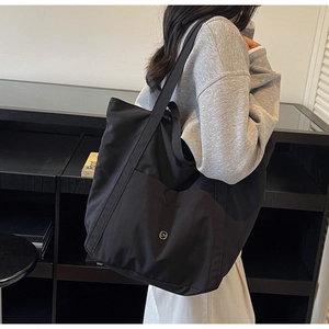 Detailed close-up of black canvas tote bag showing large front pocket and metal logo charm