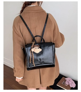 Close-up of black glossy leather backpack with cute teddy bear charm and logo detail
