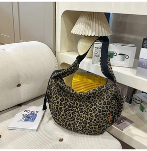 Gros plan d'un sac bandoulière en toile léopard avec large sangle noire sur canapé